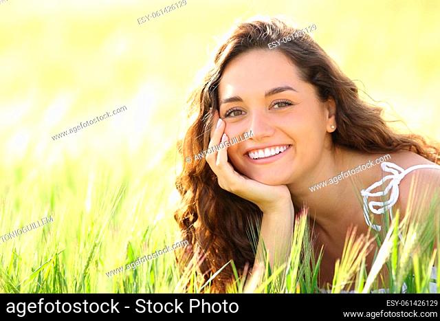 Portrait of a happy woman with perfect smile sitting in a wheat field looking at you