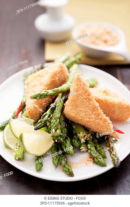 Breaded tofu on a bed of green asparagus with lime wedges
