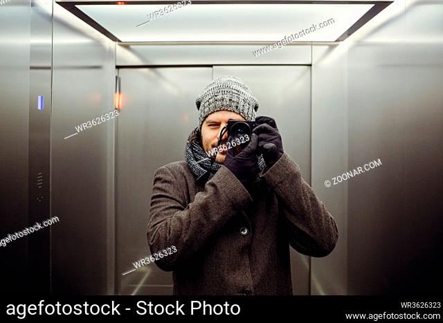 Male photographer taking a self picture in an elevator. Mirror selfie portrait, learning photography and analog film look concept