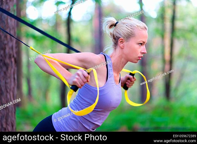 Young attractive woman does suspension training with fitness straps outdoors in the nature