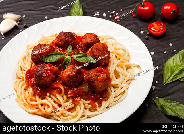 Spaghetti pasta with meatballs and tomato sauce on black background