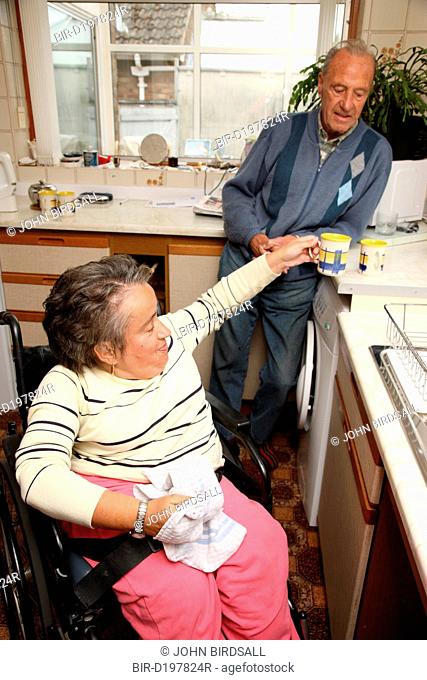 Wheelchair user with Spina Bifida doing washing up while her father watches