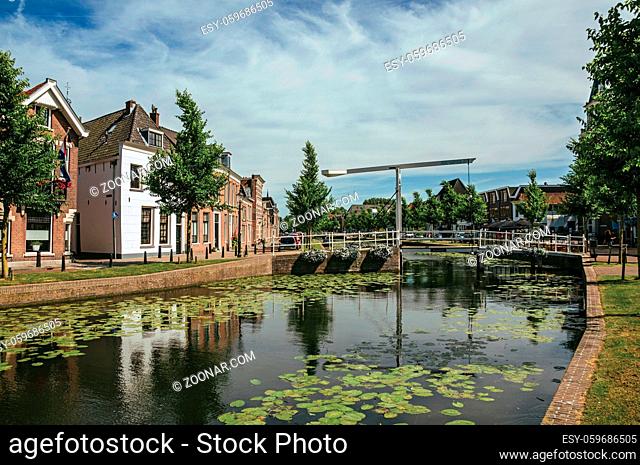 Tree-lined canal with aquatic plants, streets on the banks, brick houses and bascule bridge on a sunny day in Weesp. Pleasant village full of canals and green...