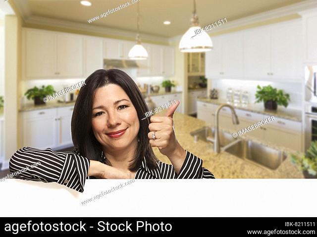 Smiling hispanic woman with thumbs up in beautiful custom kitchen