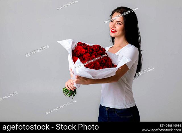 beautiful smiling young woman holding large bouquet of red roses on gray background. flower delivery