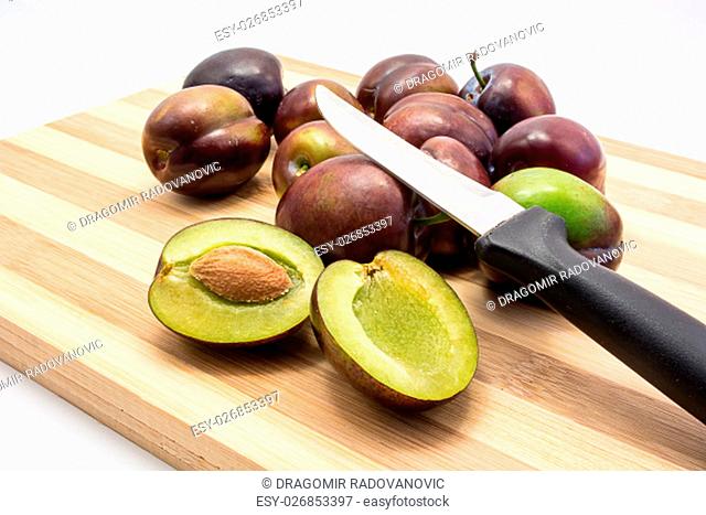 Juicy plum cuted in half on wooden board. Group of plums visible. Isolated on white background