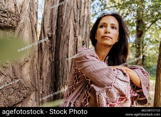 Woman looking away while sitting under Robinia Pseudoacacia tree at park