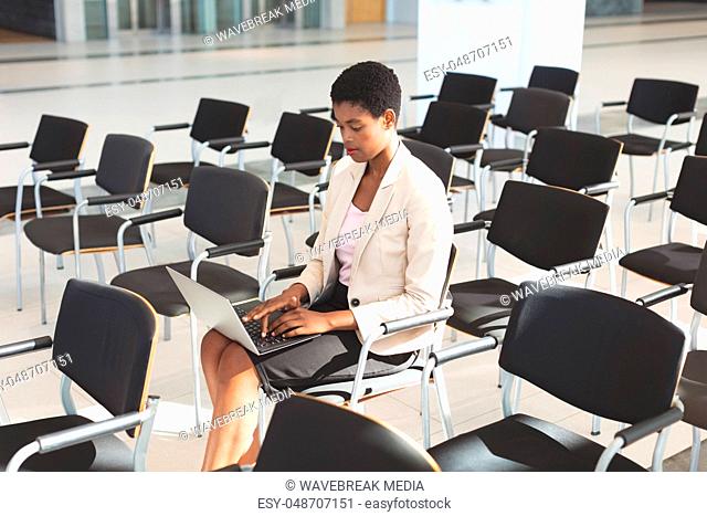 Businesswoman sitting on chair and using laptop in lobby