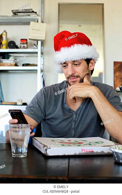 Portrait of mid adult man wearing santa hat looking at cellphone