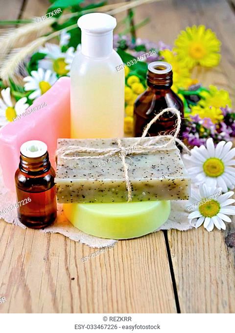 Oil and lotion bottles, homemade soap on a piece of paper, chamomile flowers, tansy, elecampane on the background of wooden boards
