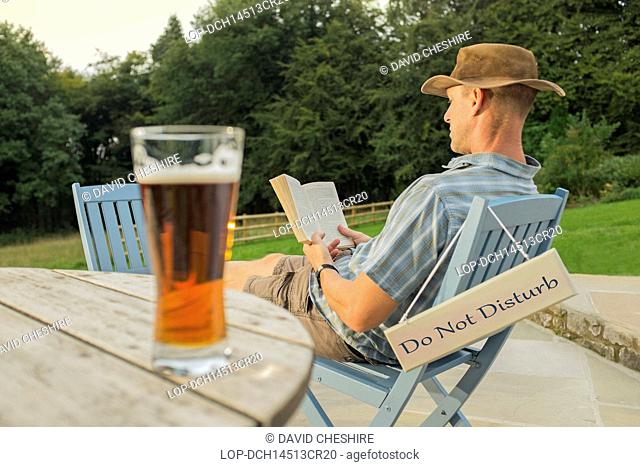 Wales, Monmouthshire, Monmouth. A man relaxing with a book and glass of beer