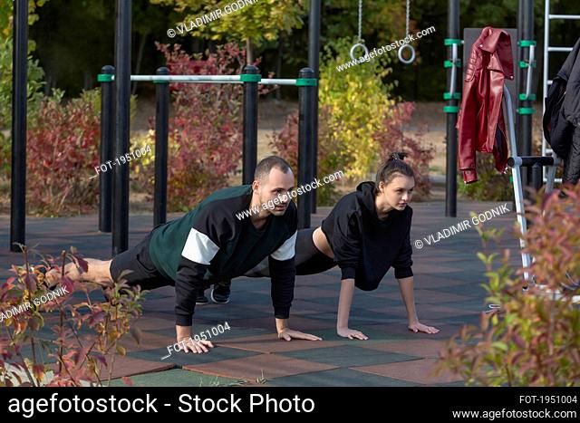 Athletic young couple doing plank exercises at park playground