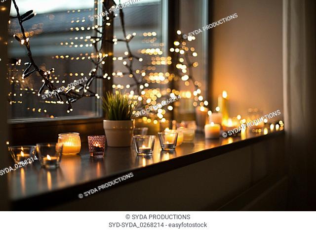 candles burning on window sill with garland lights