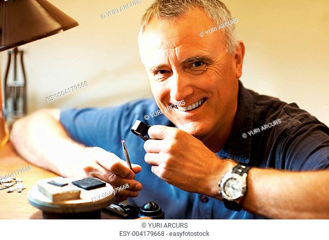Happy jeweler looking at a gem in his workplace