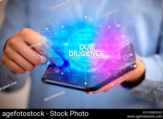 Businessman holding a foldable smartphone with DUE DILIGENCE inscription, new business concept