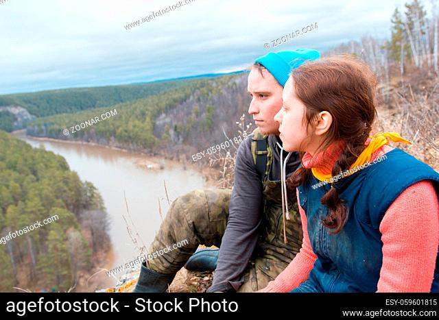 Young caucasian couple sitting the hillside to the river, telephoto shot