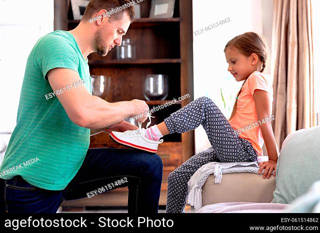 Caucasian girl sitting on a couch while her dad is helping her putting on shoes