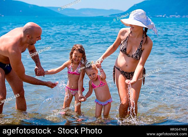 young happy couple with cute little daughters having fun while splashing each other in the shallow water of the sea during Summer vacation Healthy family...
