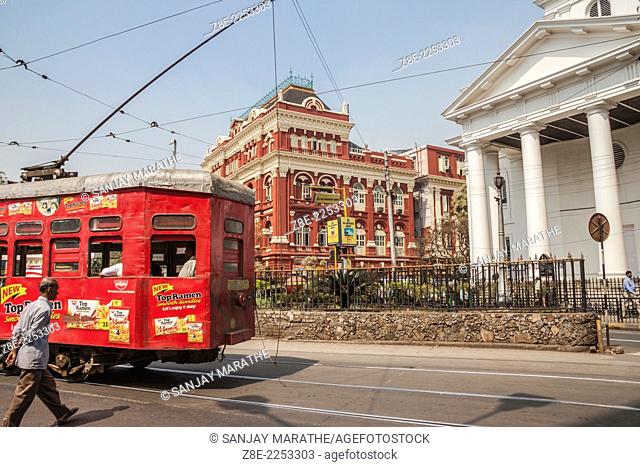 A red tram passes along the busy BBD Bagh (Dalhousie square) area, with the red Writers Buildings and St. Andrew's Church in the background
