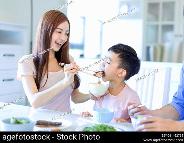little boy enjoy eating food with father and mother. Happy Asian family having dinner at home