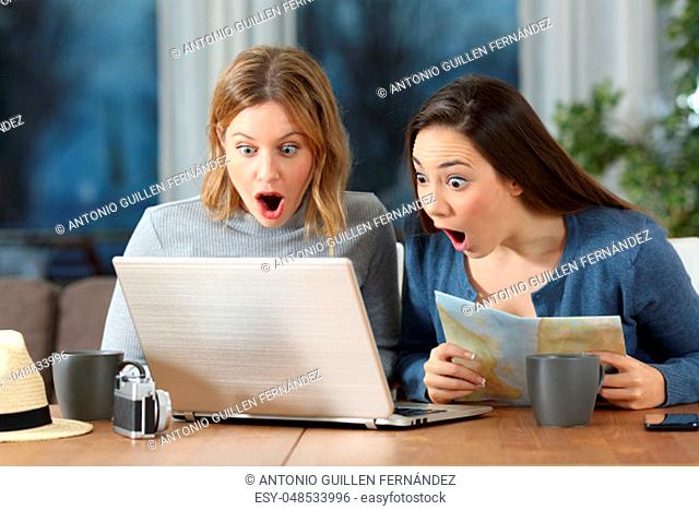 Two amazed tourists finding offers on line during a travel in an apartment in the evening