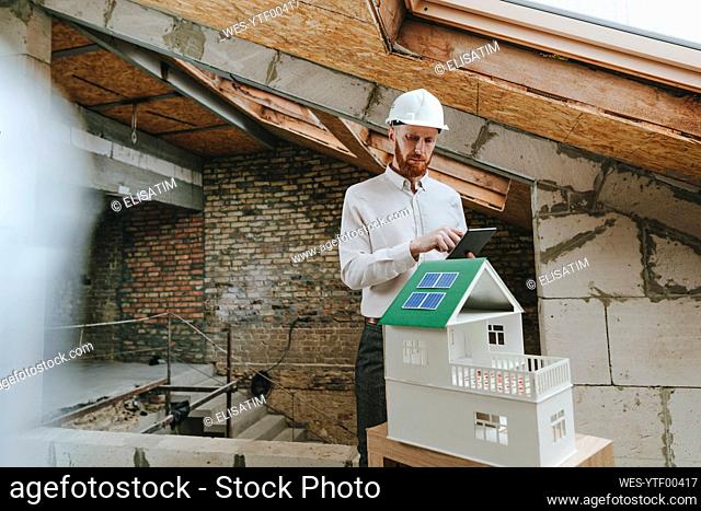 Architect analyzing house model using tablet PC at construction side