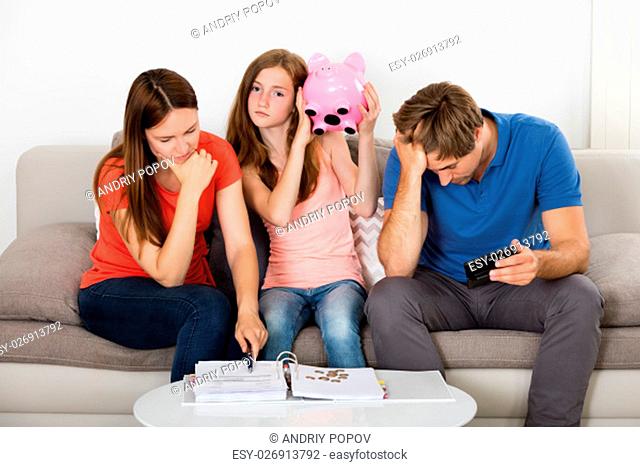 Girl Sitting On Sofa With Her Unhappy Parent Shaking Piggybank