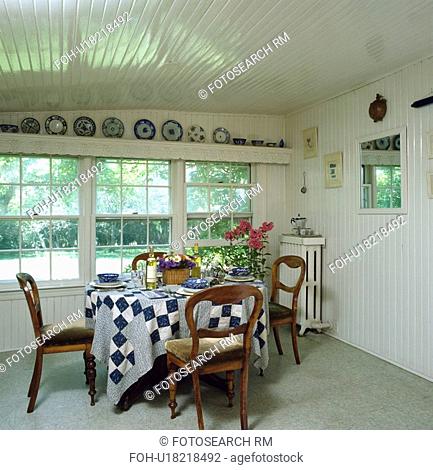 Blue+white patchwork cloth on table in front of window white country dining room with white timbered ceiling and walls