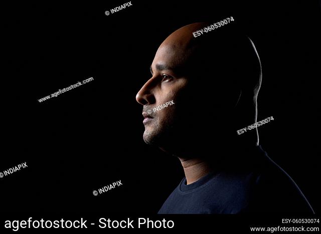 Portrait of a bald man with serious expression against dark black background