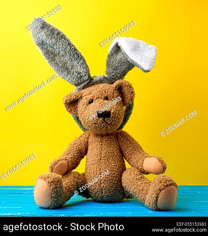 cute brown teddy bear wearing a rabbit mask with long ears on his head, funny holiday Easter card