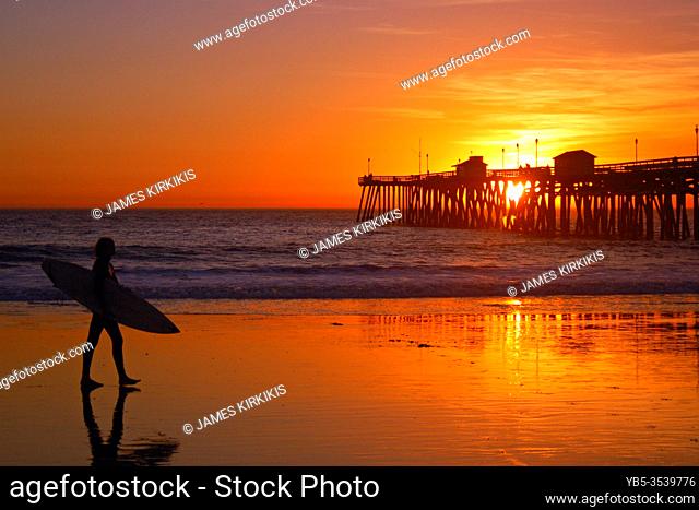 A surfer walks his board back from the ocean at sunset in San Clemente, California