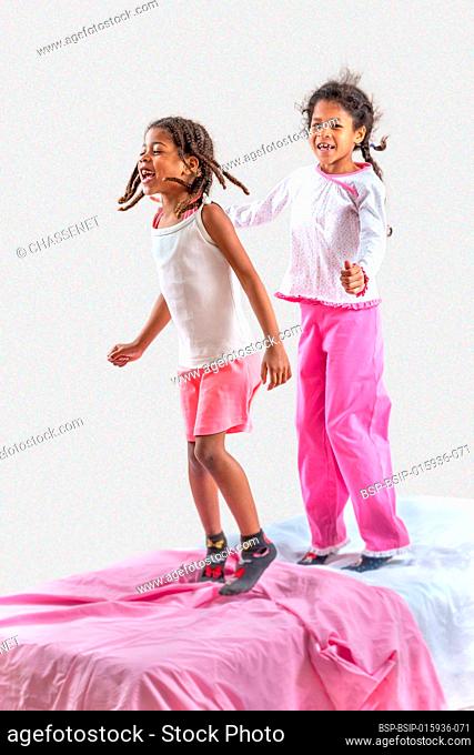 Two little girls jumping in the bed