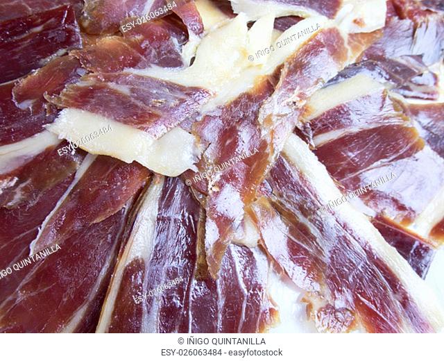 pile of typical spanish iberico ham sliced on white dish