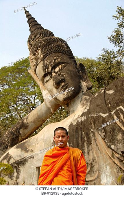 Buddhist monk wearing an orange robe in front of a Reclining Buddha statue, Buddha Park, Suan Xieng Khuan, near Vientiane, Laos, Southeast Asia