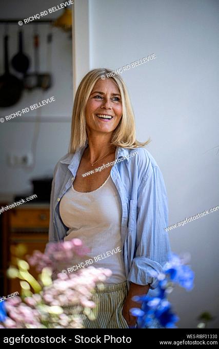 Smiling mature woman with blond hair standing at home