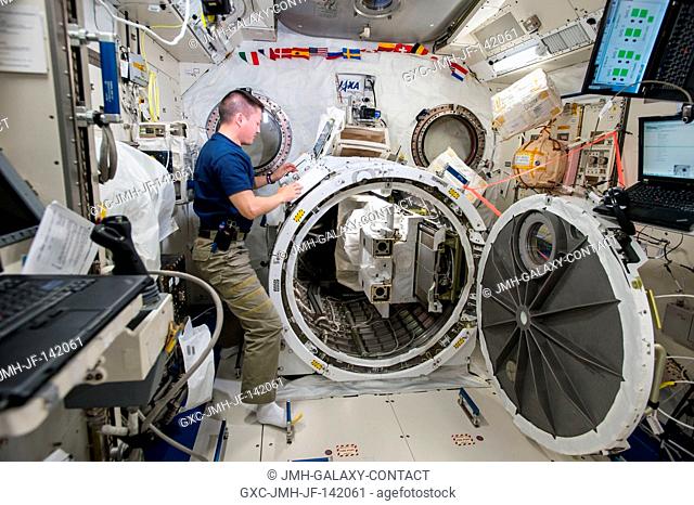 NASA astronaut Kjell Lindgren loads a deployer device filled with 16 CubeSats into a small airlock in the Japanese Kibo Module on the International Space...