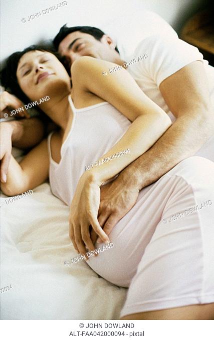 Couple lying together on bed, both touching woman's pregnant belly