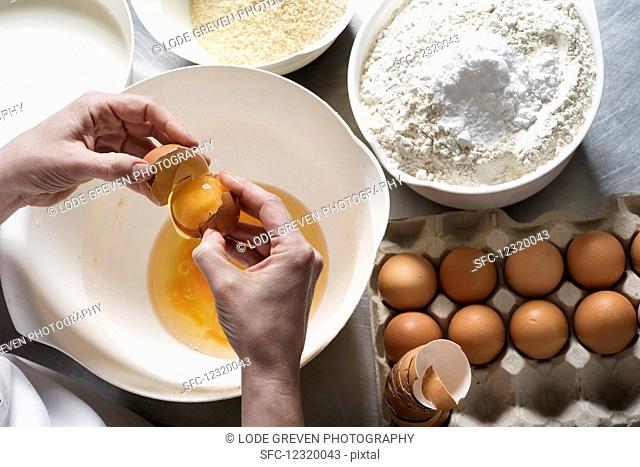 Hands breaking eggs over a bowl with almond flour and regular flour with baking powder next to it
