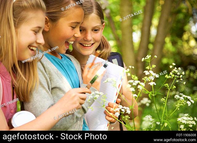 Smiling girls with magnifying glass examining flowers on field trip
