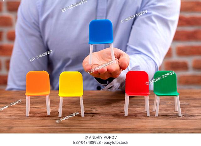 Person's Hand Holding Blue Chair Near Colorful Chairs On Desk