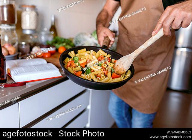 MIdsection of man preparing pasta while standing in kitchen at home