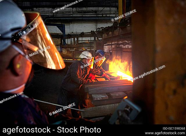 100mm square steel billet is removed from furnace as cold steel billet waits to be heated, with furnace door operator in foreground