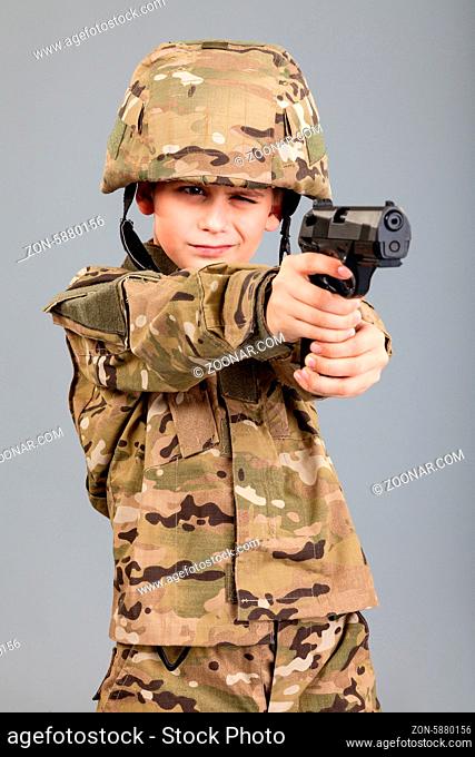 Young boy dressed like a soldier with a gun isolated on gray background