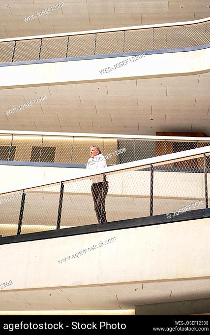 Businessman leaning on railing in corridor of office