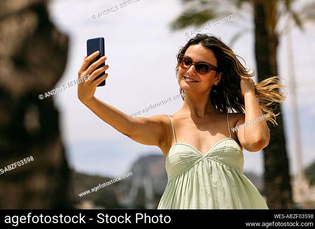 Mid adult woman with hand in hair taking selfie through smart phone