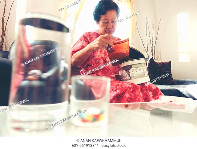 Senior asian woman take pill medicine on hand while sitting on sofa at home