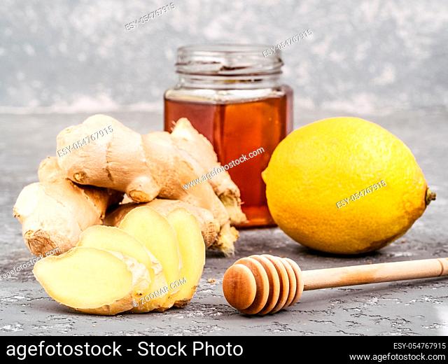 Close up view of ginger slice, ginger root, lemon and honey on gray concrete background