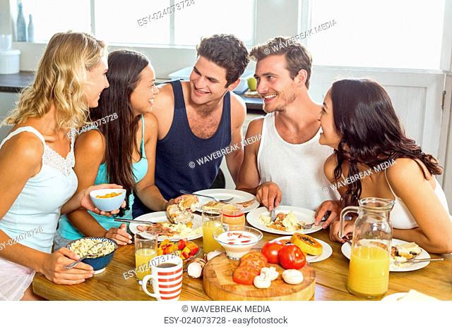 Smiling young friends having breakfast at table in house