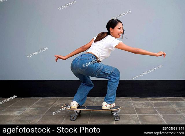 Young asian woman with sunglasses on her head surfing skateboard on pedestrian lane