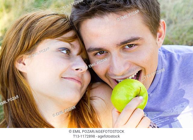 Girl is feeding a boy with a Green apple